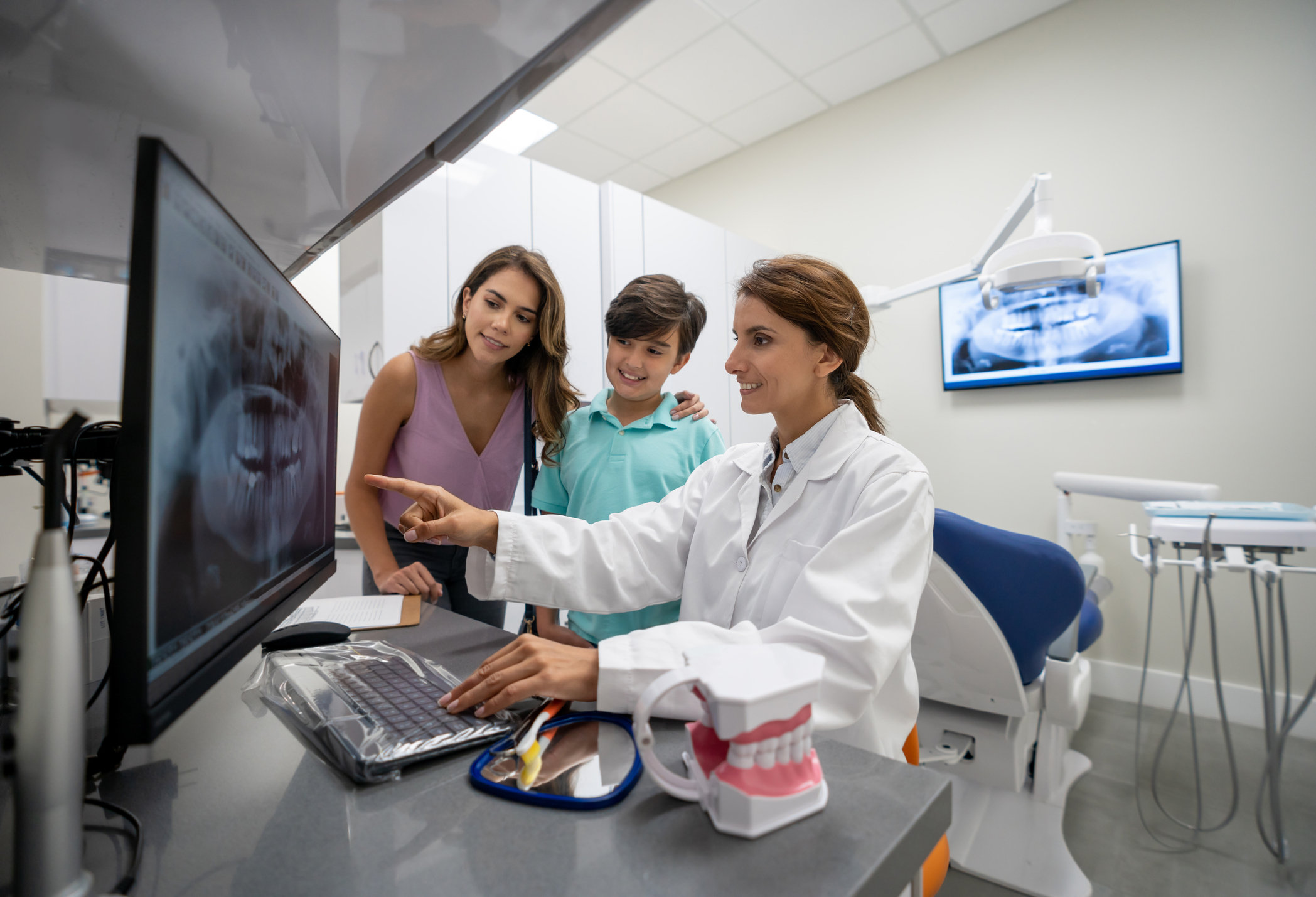 Latin American boy with his mother at the dentist looking at an x-ray of his teeth on a computer screen - healthcare and medicine