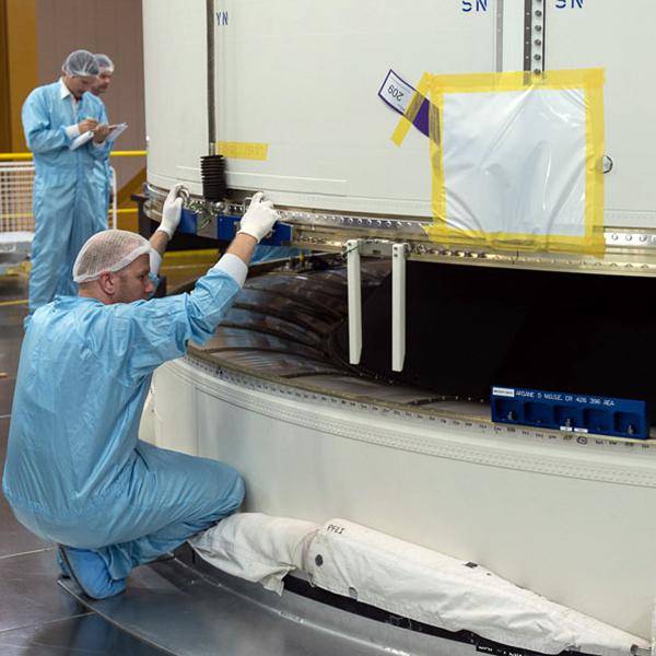 An employee is working inside a factory on part of a rocket while another employee makes notes