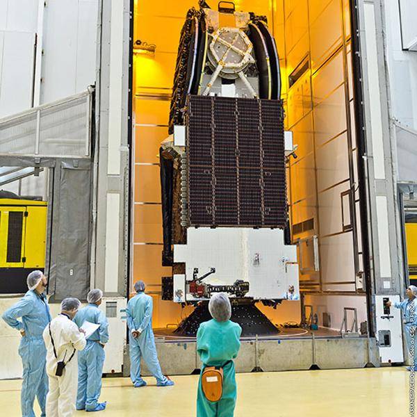 The inside of a rocket is hanging in its factory with employees nearby