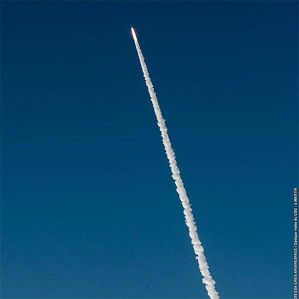 A recently launched rocket is shooting up across the blue sky with a trail of smoke showing its trajectory so far